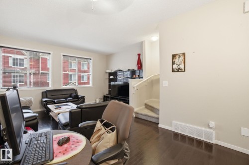 The main living area features dark wood flooring, light-colored walls, and two windows with blinds - 75 603 Watt Boulevard, Edmonton, AB - Indoor