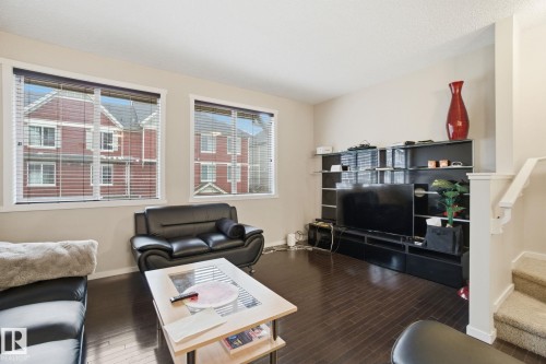 Living area featuring dark hardwood floors, two windows with blinds, and a staircase with carpeting - 75 603 Watt Boulevard, Edmonton, AB - Indoor Photo Showing Living Room