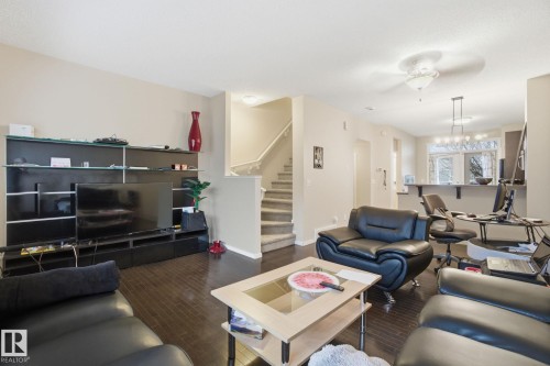 The living area features dark wood flooring, light-colored walls, and a staircase with carpeted treads - 75 603 Watt Boulevard, Edmonton, AB - Indoor Photo Showing Living Room