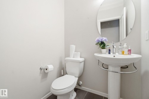 Bathroom featuring a pedestal sink, a circular mirror, and a toilet - 75 603 Watt Boulevard, Edmonton, AB - Indoor Photo Showing Bathroom