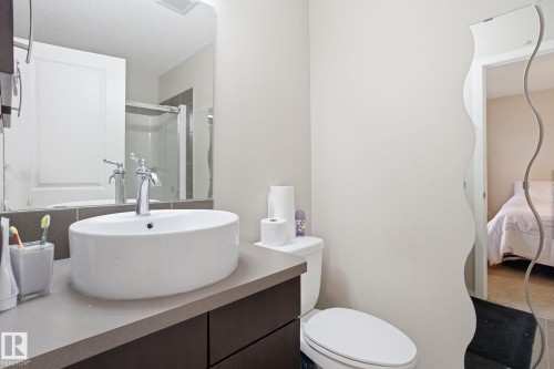 The bathroom features a vessel sink set on a vanity with a grey countertop, a toilet, and a large wall mirror - 75 603 Watt Boulevard, Edmonton, AB - Indoor Photo Showing Bathroom