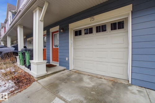 The property features blue siding, a white garage door with windows, and a front entry with an orange door - 75 603 Watt Boulevard, Edmonton, AB - Outdoor With Exterior