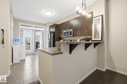 The kitchen features dark wood cabinetry, a stainless steel microwave, and a black refrigerator - 75 603 Watt Boulevard, Edmonton, AB - Indoor Photo Showing Kitchen