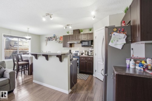 The property features an open concept kitchen and dining area, complete with dark wood cabinetry, a breakfast bar, and stainless steel appliances including a refrigerator, microwave, and dishwasher - 3026 16A Avenue, Edmonton, AB - Indoor Photo Showing Kitchen