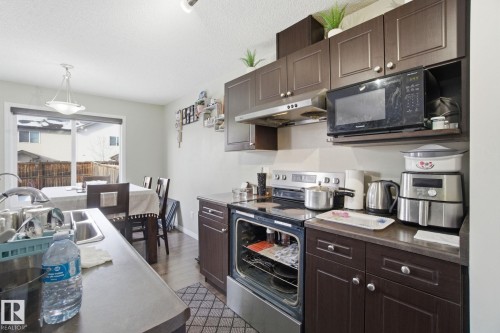 The kitchen features dark wood cabinetry, a stainless steel oven and microwave, and a double basin sink - 3026 16A Avenue, Edmonton, AB - Indoor Photo Showing Kitchen