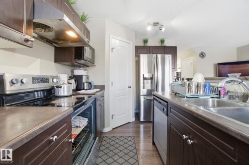 The kitchen features dark wood cabinetry, stainless steel appliances including a refrigerator and dishwasher, and a double basin sink - 3026 16A Avenue, Edmonton, AB - Indoor Photo Showing Kitchen With Stainless Steel Kitchen With Double Sink