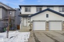 The property features a white exterior with dark blue trim, a paved driveway, and two white garage doors with stone accents - 3026 16A Avenue, Edmonton, AB  - Outdoor With Facade 