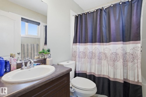 Bathroom featuring a vanity with an integrated sink and a chrome faucet, a toilet, and a shower with a decorative curtain - 3026 16A Avenue, Edmonton, AB - Indoor Photo Showing Bathroom