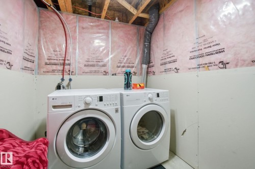 This utility area features exposed wooden ceiling beams and insulation, with a washer and dryer present - 3026 16A Avenue, Edmonton, AB - Indoor Photo Showing Laundry Room