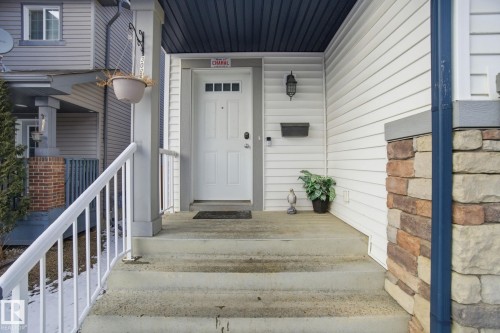 Inviting front entrance with a white door featuring decorative glass inserts, complemented by white siding and a stone facade detail - 3026 16A Avenue, Edmonton, AB - Outdoor With Exterior