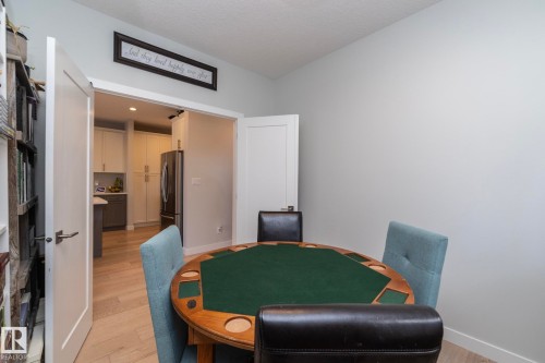 This space features light-colored walls and flooring, with a partial view into a kitchen area with white cabinetry and a stainless steel refrigerator - 26 Ellice Bend, Fort Saskatchewan, AB - Indoor Photo Showing Dining Room