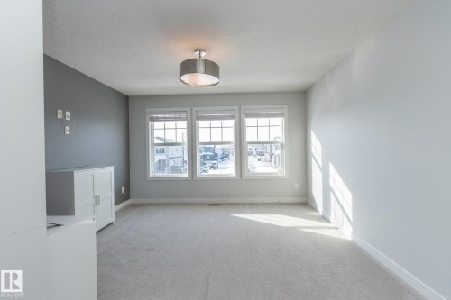 This bright room features three large windows, light gray carpeting, and a modern drum pendant light fixture - 26 Ellice Bend, Fort Saskatchewan, AB - Indoor Photo Showing Other Room