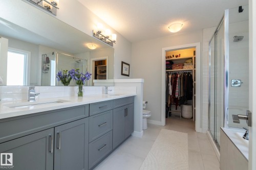 Well-appointed bathroom featuring a double vanity with gray cabinetry and white countertops, a large mirror, and a glass-enclosed shower - 26 Ellice Bend, Fort Saskatchewan, AB - Indoor Photo Showing Bathroom