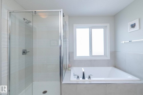 The bathroom features a glass-enclosed shower with a chrome shower head and a built-in bathtub with a window above - 26 Ellice Bend, Fort Saskatchewan, AB - Indoor Photo Showing Bathroom
