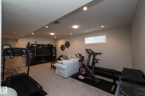 The property features a spacious room with light-colored carpeting, recessed lighting, and a window with blinds - 26 Ellice Bend, Fort Saskatchewan, AB - Indoor Photo Showing Gym Room