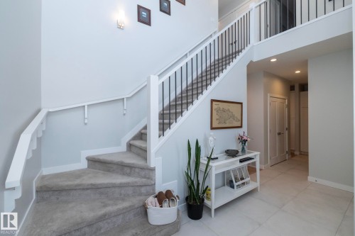 The property features a staircase with carpeted steps and a white railing, complemented by a white console table on a tiled floor - 26 Ellice Bend, Fort Saskatchewan, AB - Indoor Photo Showing Other Room