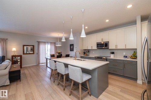 The open concept living area features light-toned hardwood floors, a kitchen with two-tone cabinetry, stainless steel appliances, and a central island with countertop seating - 26 Ellice Bend, Fort Saskatchewan, AB - Indoor Photo Showing Kitchen With Double Sink