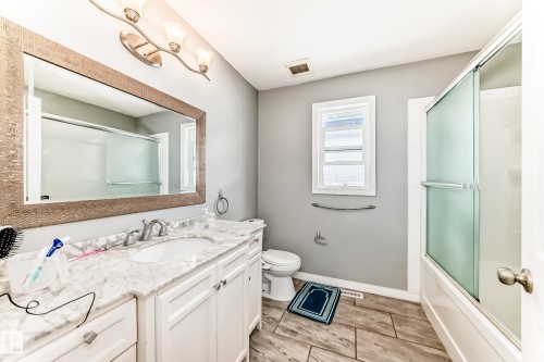 This bathroom features a spacious vanity with a marble countertop and white cabinetry, complemented by a large mirror and a light fixture with three sconces - 16720 61 Street, Edmonton, AB - Indoor Photo Showing Bathroom