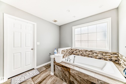 The bathroom features a built-in bathtub with a tiled surround and a mosaic tile backsplash - 16720 61 Street, Edmonton, AB - Indoor Photo Showing Bathroom