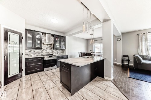 Well-appointed kitchen featuring dark cabinetry, a stylish tiled backsplash, and stainless steel appliances - 16720 61 Street, Edmonton, AB - Indoor