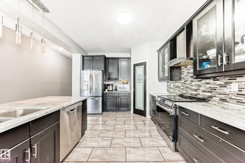 The kitchen features dark cabinetry, stainless steel appliances, a tile backsplash, and light-colored countertops - 16720 61 Street, Edmonton, AB - Indoor Photo Showing Kitchen With Upgraded Kitchen