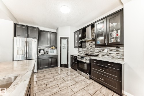 The kitchen features dark cabinetry, stainless steel appliances, and a mosaic tile backsplash - 16720 61 Street, Edmonton, AB - Indoor Photo Showing Kitchen With Upgraded Kitchen