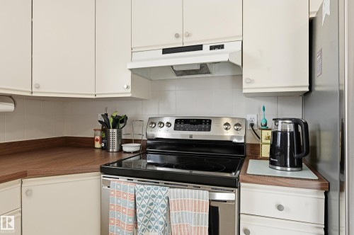 The kitchen features white cabinetry, wooden countertops, a white tiled backsplash, and a stainless steel electric stove with an overhead range hood - 85 Arlington Drive, St. Albert, AB - Indoor Photo Showing Kitchen
