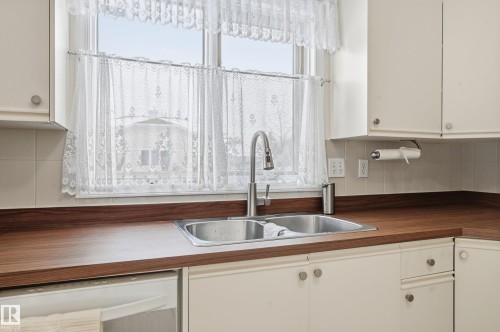 Kitchen featuring a double stainless steel sink with a modern faucet, wood-look countertops, and white cabinetry - 85 Arlington Drive, St. Albert, AB - Indoor Photo Showing Kitchen With Double Sink