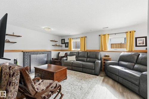 Living area featuring a brick fireplace, light-toned flooring, and wall-mounted shelving - 85 Arlington Drive, St. Albert, AB - Indoor Photo Showing Living Room