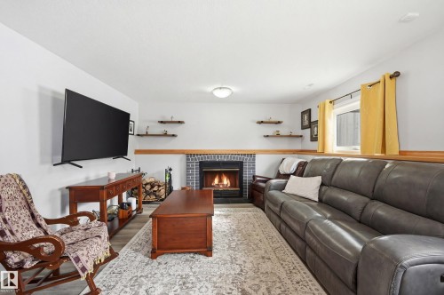Living area featuring a fireplace with a dark brick surround, a window with yellow curtains, and light-colored walls - 85 Arlington Drive, St. Albert, AB - Indoor Photo Showing Living Room With Fireplace