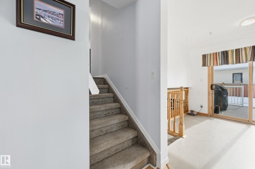 The property features a staircase with carpeted treads and a wooden railing, alongside a room with a sliding glass door leading to an outdoor deck - 85 Arlington Drive, St. Albert, AB - Indoor Photo Showing Other Room