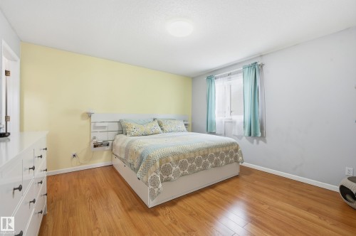 The property features polished hardwood floors, light-colored walls, and a window with curtains - 85 Arlington Drive, St. Albert, AB - Indoor Photo Showing Bedroom