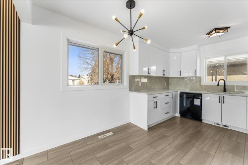 The kitchen features white cabinetry with black hardware, a black dishwasher, a black faucet, and a grey backsplash - 13116 128A Avenue, Edmonton, AB - Indoor Photo Showing Kitchen