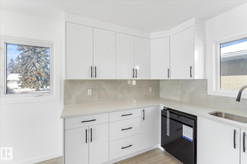 The kitchen features white cabinetry with black handles, light-toned countertops, and a complementary backsplash - 13116 128A Avenue, Edmonton, AB - Indoor Photo Showing Kitchen