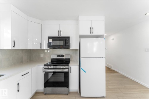 The kitchen features white cabinetry, a stainless steel electric stove with a matching microwave, and a white refrigerator - 13116 128A Avenue, Edmonton, AB - Indoor Photo Showing Kitchen