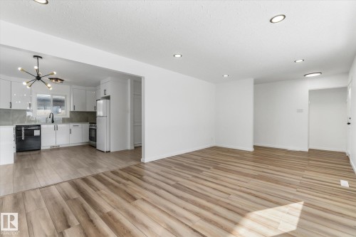 The property features a bright living area with plank flooring and recessed lighting, opening into a kitchen with white cabinetry, a modern light fixture, and stainless steel appliances - 13116 128A Avenue, Edmonton, AB - Indoor Photo Showing Kitchen