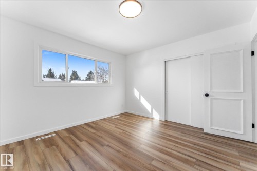 This room features light wood-style flooring, a spacious window with a view of trees and other buildings, and a ceiling-mounted light fixture - 13116 128A Avenue, Edmonton, AB - Indoor Photo Showing Other Room