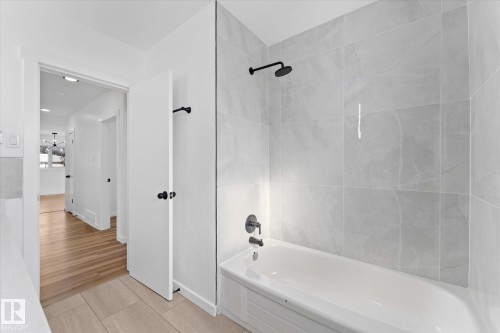 Bathroom featuring a bathtub with a shower, light grey tiled walls, and matte black fixtures - 13116 128A Avenue, Edmonton, AB - Indoor Photo Showing Bathroom