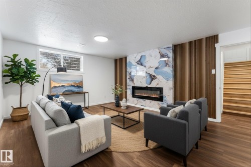 Living area featuring rich wood-toned flooring, a unique accent wall with patterned panels and integrated fireplace, and a light-colored ceiling - 13116 128A Avenue, Edmonton, AB - Indoor Photo Showing Living Room With Fireplace