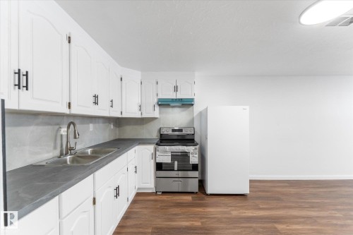 The kitchen features white cabinetry with dark hardware, dark countertops, and a double basin stainless steel sink with a gooseneck faucet - 13116 128A Avenue, Edmonton, AB - Indoor Photo Showing Kitchen With Double Sink