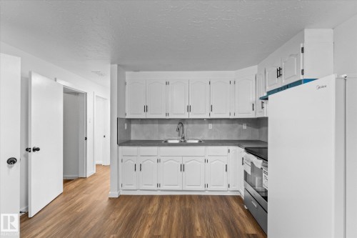 Kitchen featuring white cabinetry, a stainless steel sink with a faucet, and wood-look flooring - 13116 128A Avenue, Edmonton, AB - Indoor Photo Showing Kitchen With Double Sink