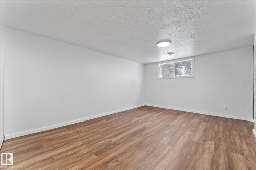 Spacious room featuring light-toned wood-style flooring, white walls, and a window with a security grate - 13116 128A Avenue, Edmonton, AB - Indoor Photo Showing Other Room