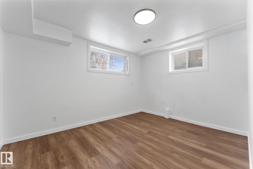 The property features white walls, durable wood-look flooring, and windows providing natural light - 13116 128A Avenue, Edmonton, AB - Indoor Photo Showing Other Room
