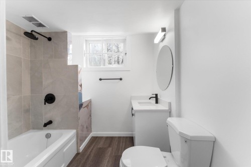 The bathroom features a bathtub with a shower, a vanity with a sink, a toilet, and a window - 13116 128A Avenue, Edmonton, AB - Indoor Photo Showing Bathroom