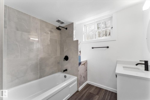 Well-appointed bathroom featuring a white bathtub with matte black fixtures, light gray tiled walls, a window providing natural light, and a vanity with a white countertop and matte black faucet - 13116 128A Avenue, Edmonton, AB - Indoor Photo Showing Bathroom