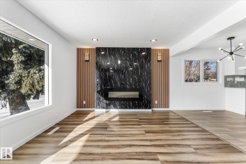 This living area features wide plank flooring, a modern black and white marbled fireplace, and recessed lighting - 13116 128A Avenue, Edmonton, AB - Indoor Photo Showing Other Room