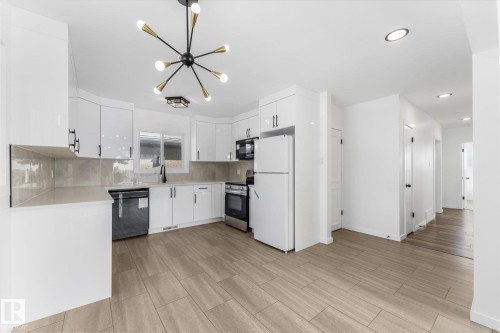 The property features a bright kitchen with white cabinetry, a stylish overhead light fixture, and a window above the sink - 13116 128A Avenue, Edmonton, AB - Indoor Photo Showing Kitchen