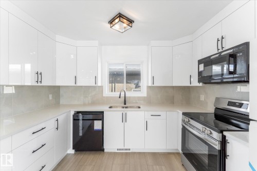 Bright kitchen featuring white cabinetry, light countertops, a window above the sink, and stainless steel appliances including a range and microwave - 13116 128A Avenue, Edmonton, AB - Indoor Photo Showing Kitchen With Double Sink With Upgraded Kitchen