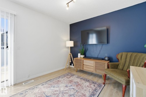 Living area featuring light wood flooring, a dark blue accent wall, and a large window with vertical blinds - 29 9619 180 Street, Edmonton, AB - Indoor