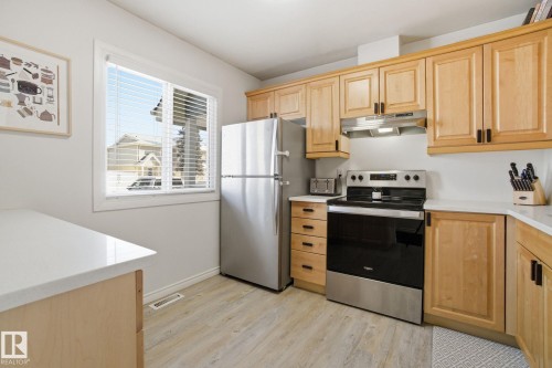 The kitchen features wood cabinetry, stainless steel appliances including a refrigerator and oven, white countertops, and a window with blinds - 29 9619 180 Street, Edmonton, AB - Indoor Photo Showing Kitchen
